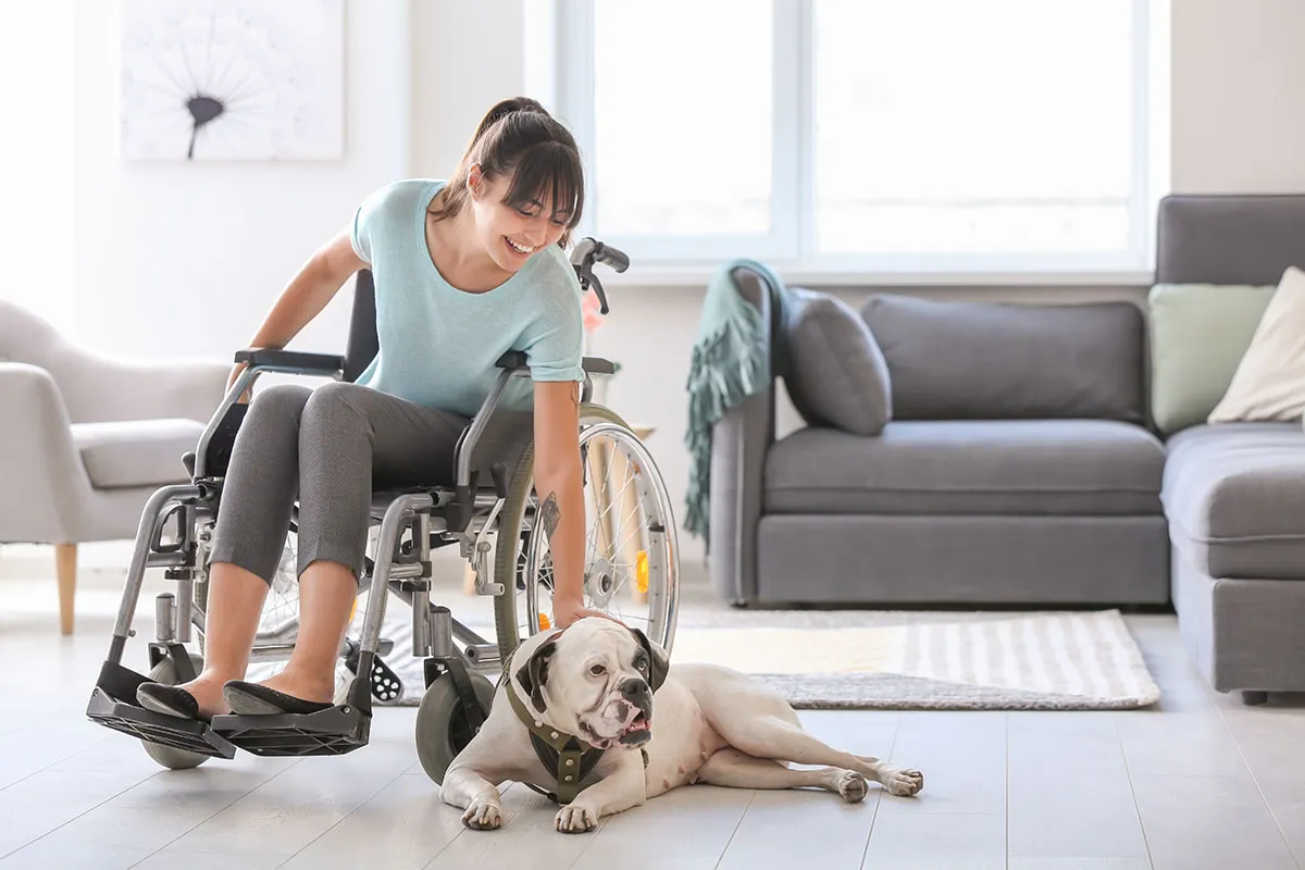 Woman in wheelchair petting her dog laying on living room floor